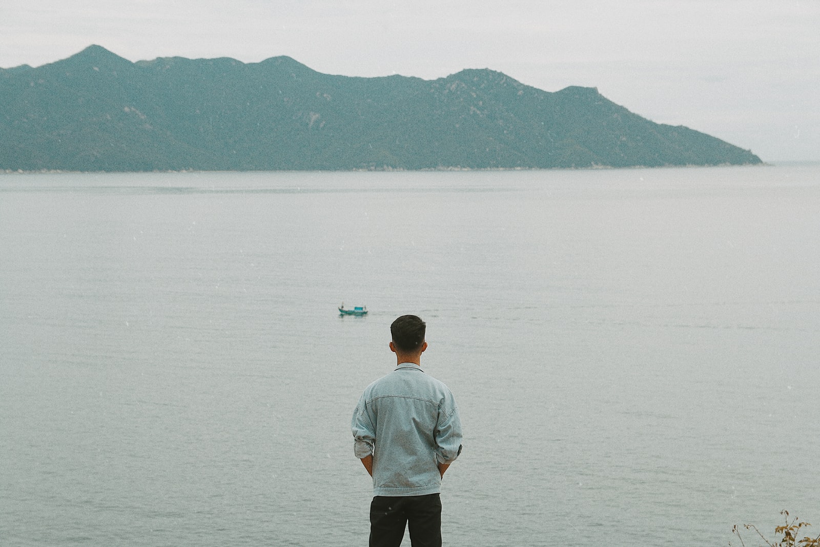 man in white shirt standing on rock in front of body of water during daytime